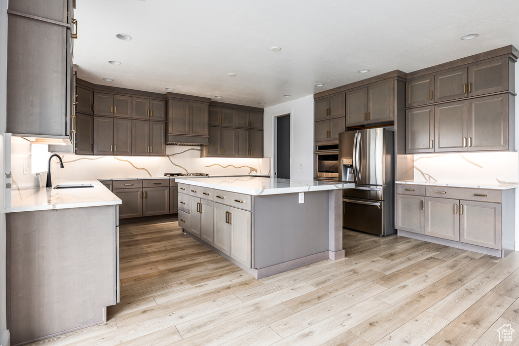 Kitchen featuring a kitchen island, appliances with stainless steel finishes, a sink, and light wood-style floors