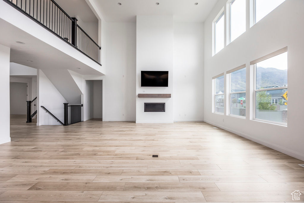 Unfurnished living room with baseboards, a high ceiling, and light wood-style flooring