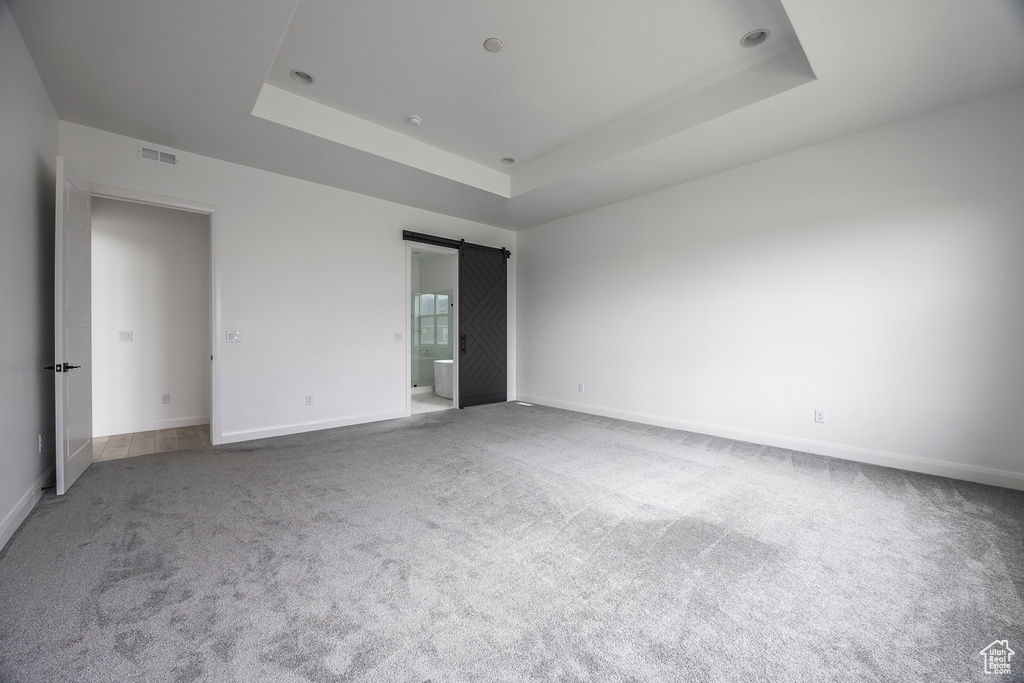 Unfurnished bedroom with visible vents, a barn door, carpet floors, and a tray ceiling