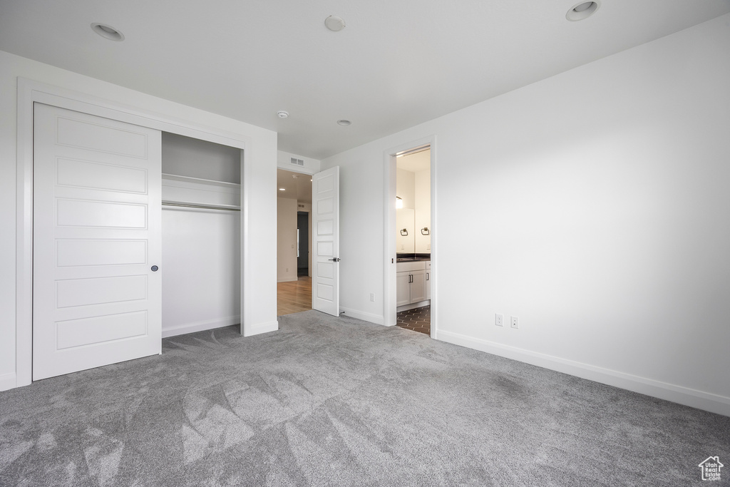 Unfurnished bedroom featuring connected bathroom, carpet floors, baseboards, visible vents, and a closet