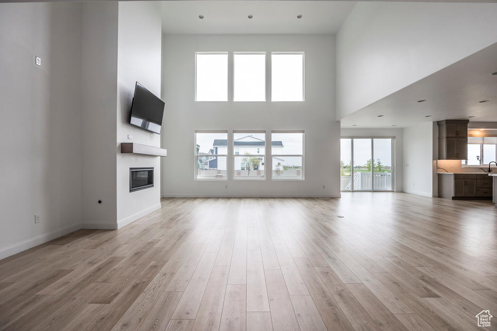 Unfurnished living room with a towering ceiling, a glass covered fireplace, baseboards, a sink, and light wood finished floors