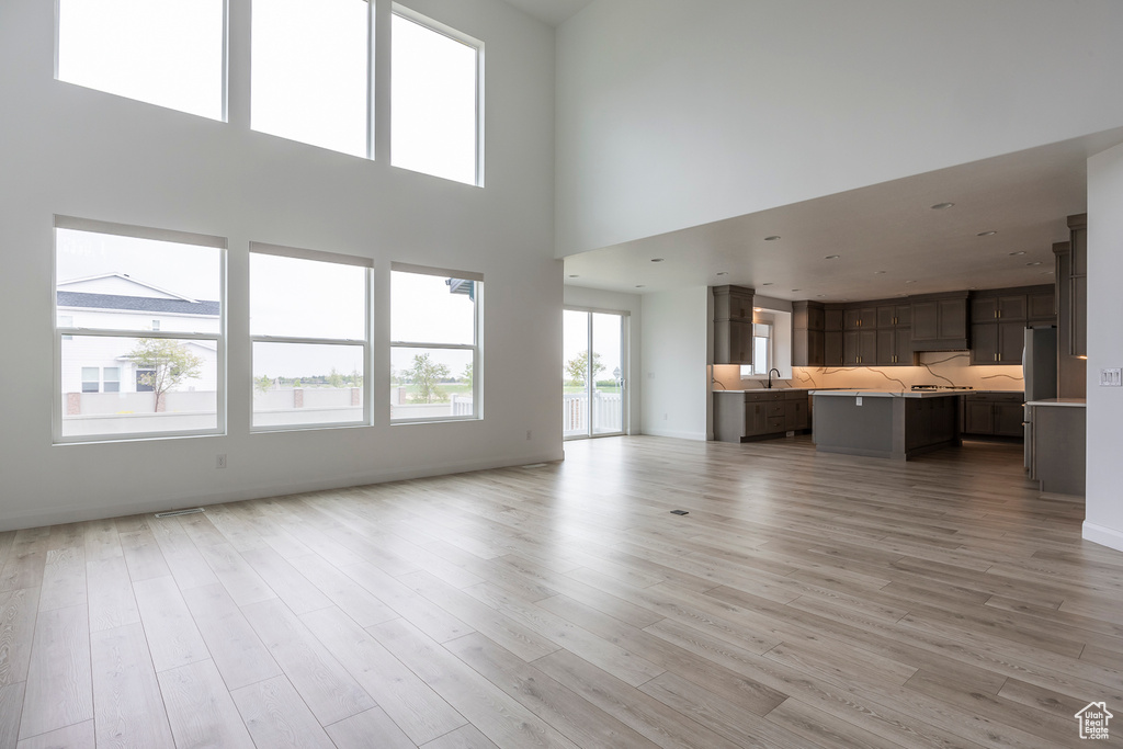 Unfurnished living room featuring baseboards, a sink, light wood finished floors, and a towering ceiling