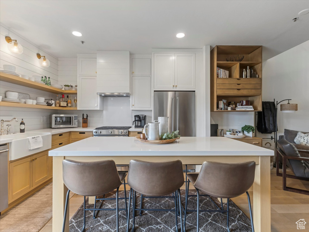 Kitchen with light countertops, open shelves, stainless steel appliances, and a kitchen bar
