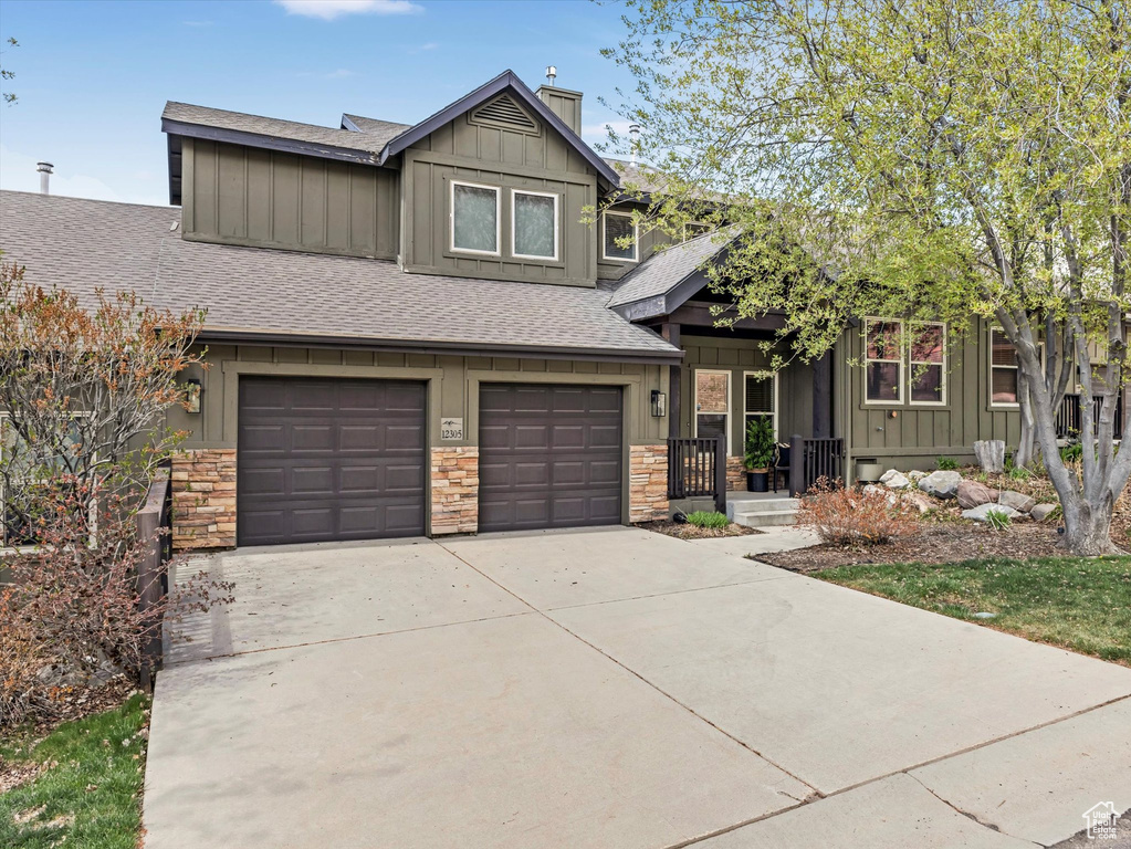 Craftsman-style home featuring roof with shingles, a chimney, board and batten siding, an attached garage, and driveway