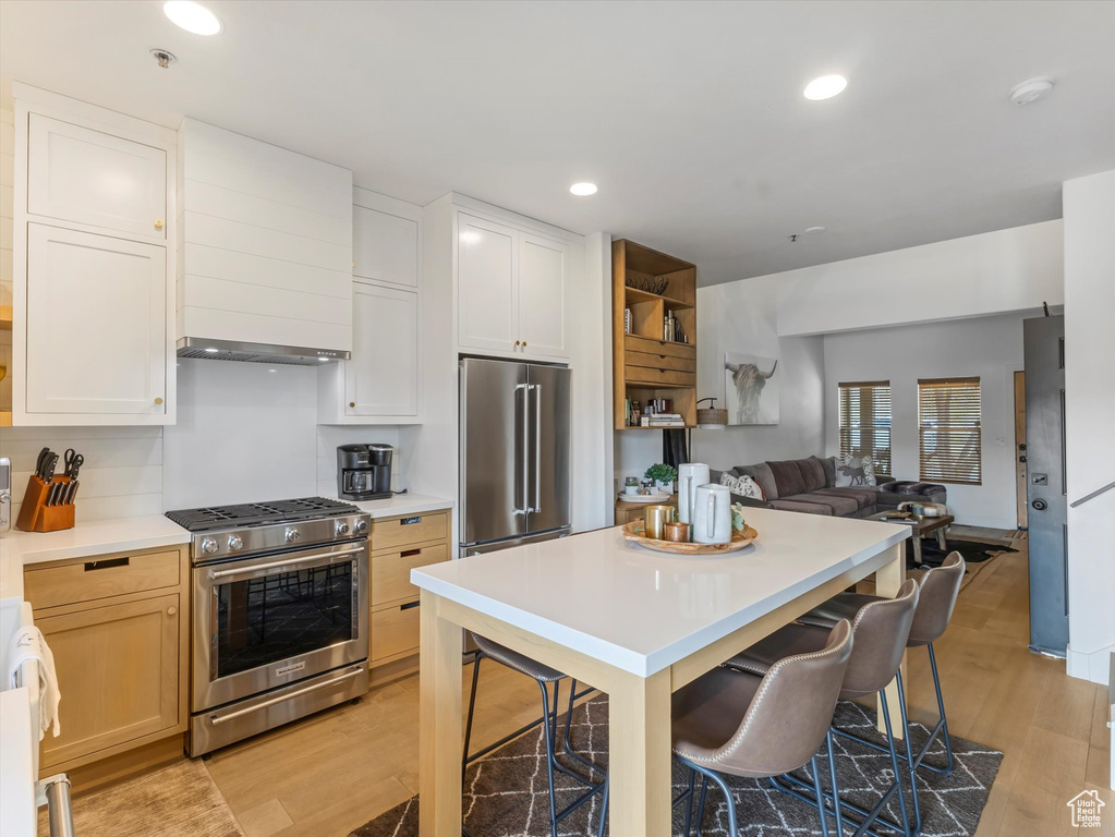 Kitchen featuring light wood-style floors, appliances with stainless steel finishes, a breakfast bar area, and wall chimney exhaust hood