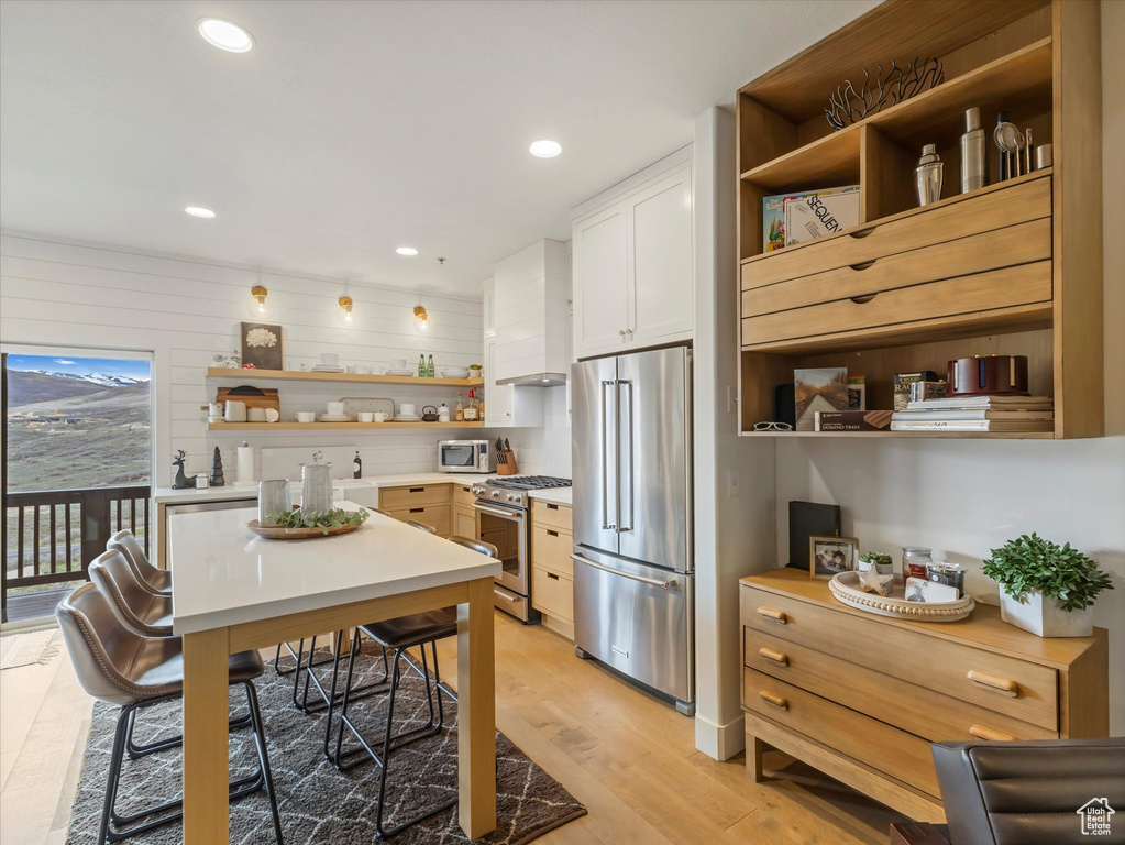 Kitchen featuring light countertops, stainless steel appliances, open shelves, and light wood-type flooring