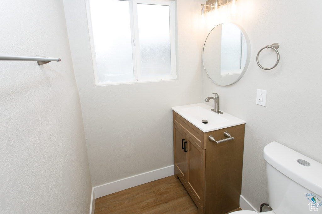 Half bathroom featuring toilet, baseboards, wood finished floors, and vanity