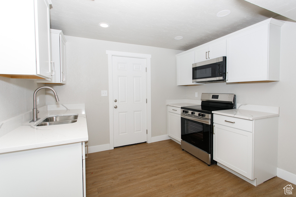Kitchen with appliances with stainless steel finishes, a sink, light countertops, light wood-style flooring, and baseboards