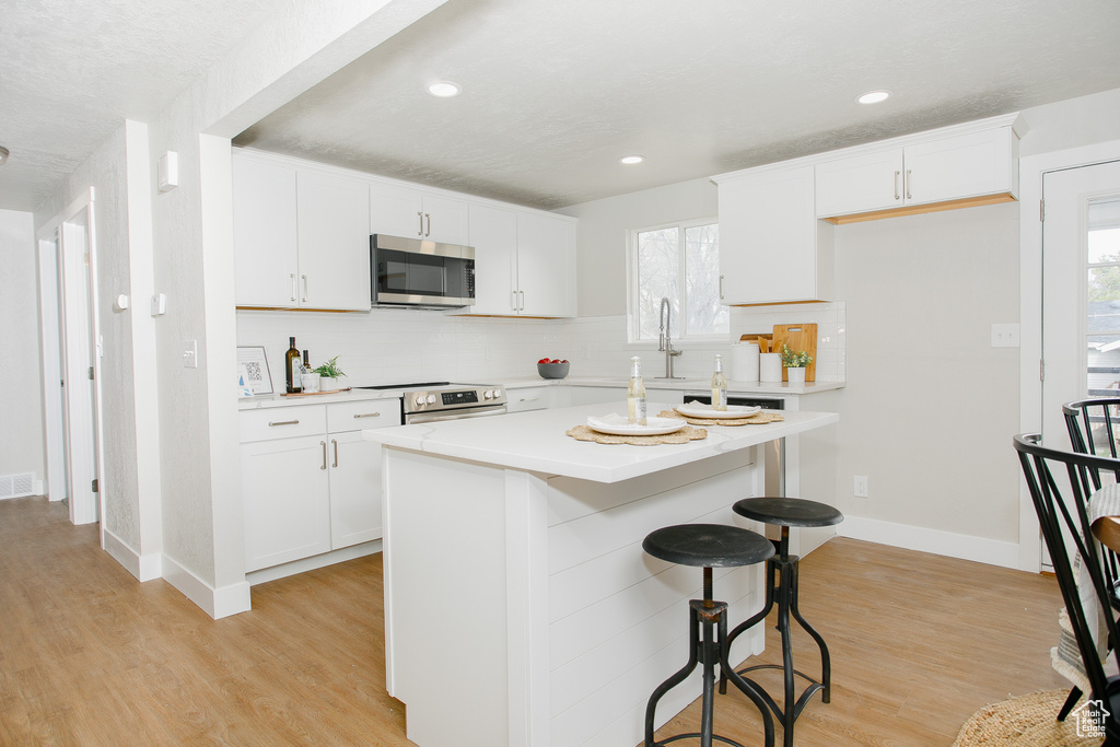 Kitchen featuring a kitchen bar, appliances with stainless steel finishes, tasteful backsplash, light countertops, and light wood-style flooring