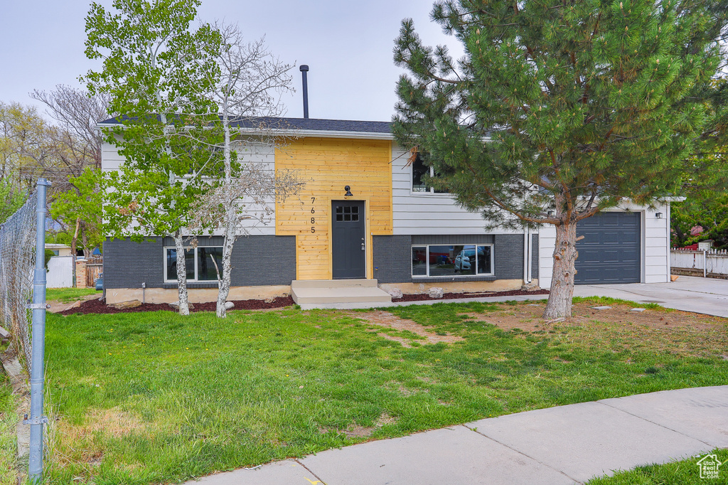 Raised ranch with fence, an attached garage, brick siding, a front yard, and driveway