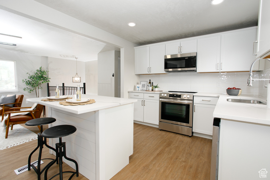 Kitchen with a kitchen island, a kitchen bar, appliances with stainless steel finishes, a sink, and light wood-style flooring