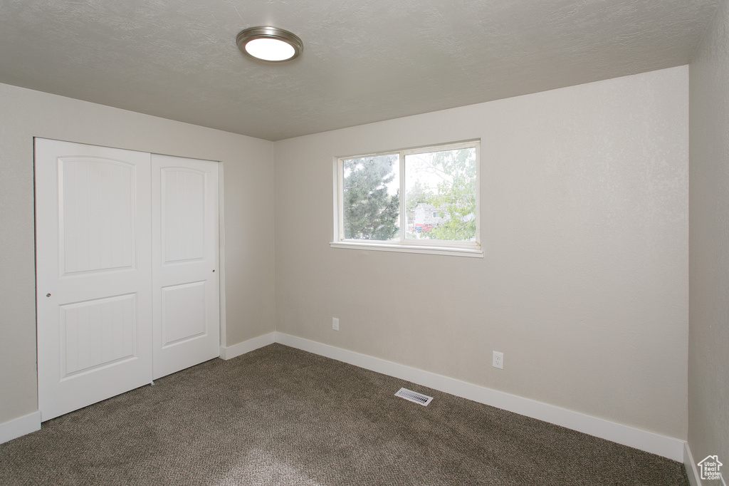 Unfurnished bedroom featuring visible vents, baseboards, a closet, and dark colored carpet