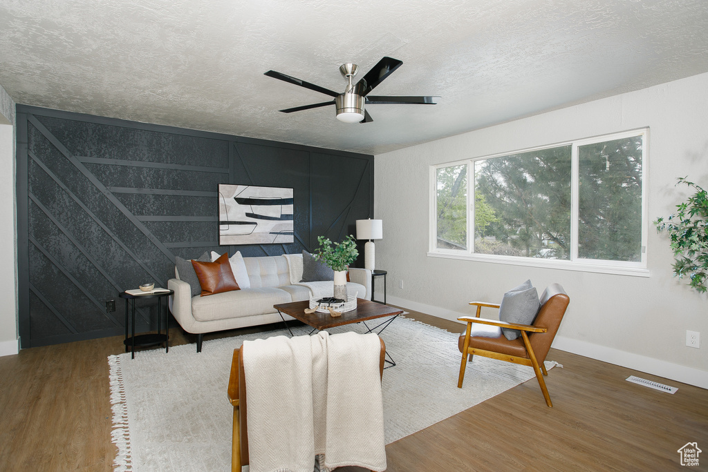 Living room featuring ceiling fan, a textured ceiling, baseboards, wood finished floors, and visible vents