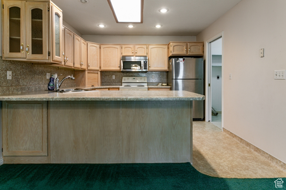 Kitchen featuring light brown cabinetry, appliances with stainless steel finishes, a sink, a peninsula, and tasteful backsplash