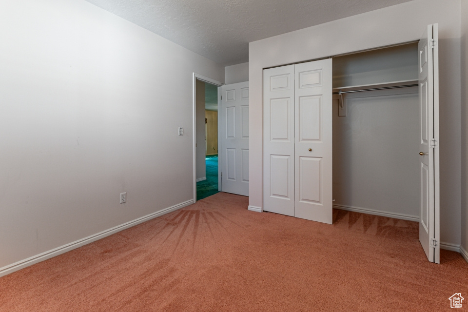Unfurnished bedroom with light colored carpet, a textured ceiling, baseboards, and a closet