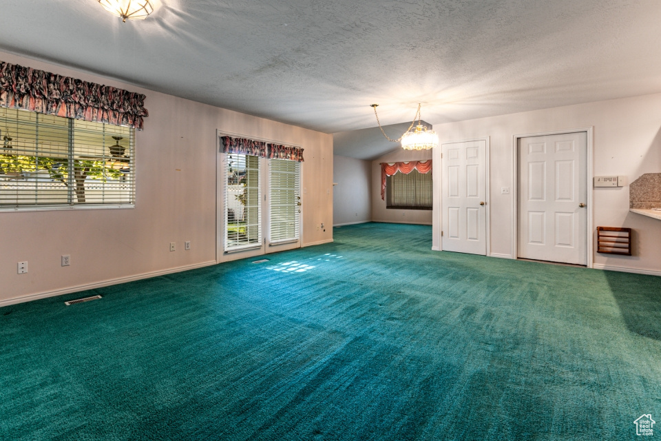 Empty room featuring an inviting chandelier, a textured ceiling, carpet, and visible vents