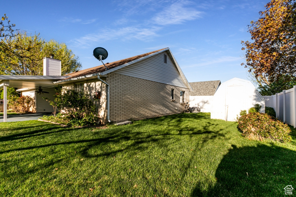 View of property exterior featuring fence, a shed, a chimney, brick siding, and a ceiling fan