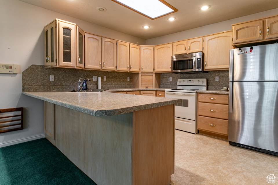Kitchen with light brown cabinetry, appliances with stainless steel finishes, a peninsula, decorative backsplash, and glass insert cabinets