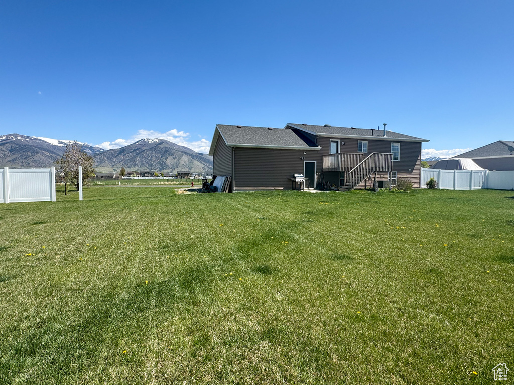 Back of house featuring a lawn, a deck with mountain view, fence, and stairs
