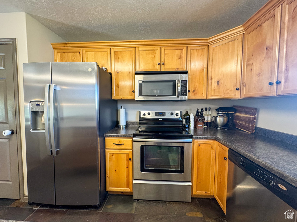 Kitchen featuring stone finish flooring, a textured ceiling, appliances with stainless steel finishes, and dark countertops