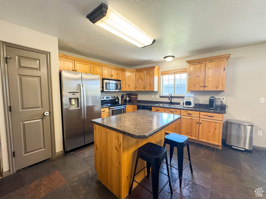 Kitchen with a kitchen breakfast bar, a kitchen island, a textured ceiling, dark countertops, and stainless steel appliances
