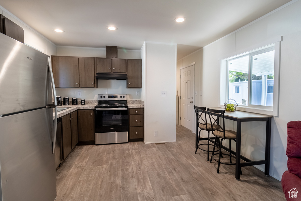 Kitchen featuring dark brown cabinetry, light countertops, under cabinet range hood, stainless steel appliances, and light wood-style flooring