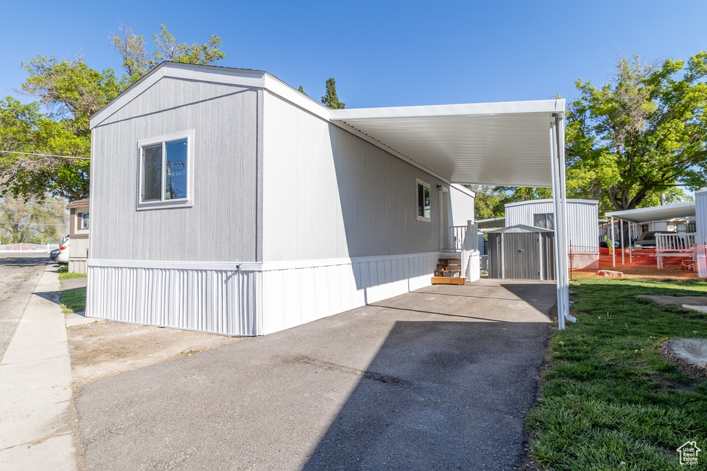 View of side of home with a storage unit, an outdoor structure, an attached carport, and aphalt driveway