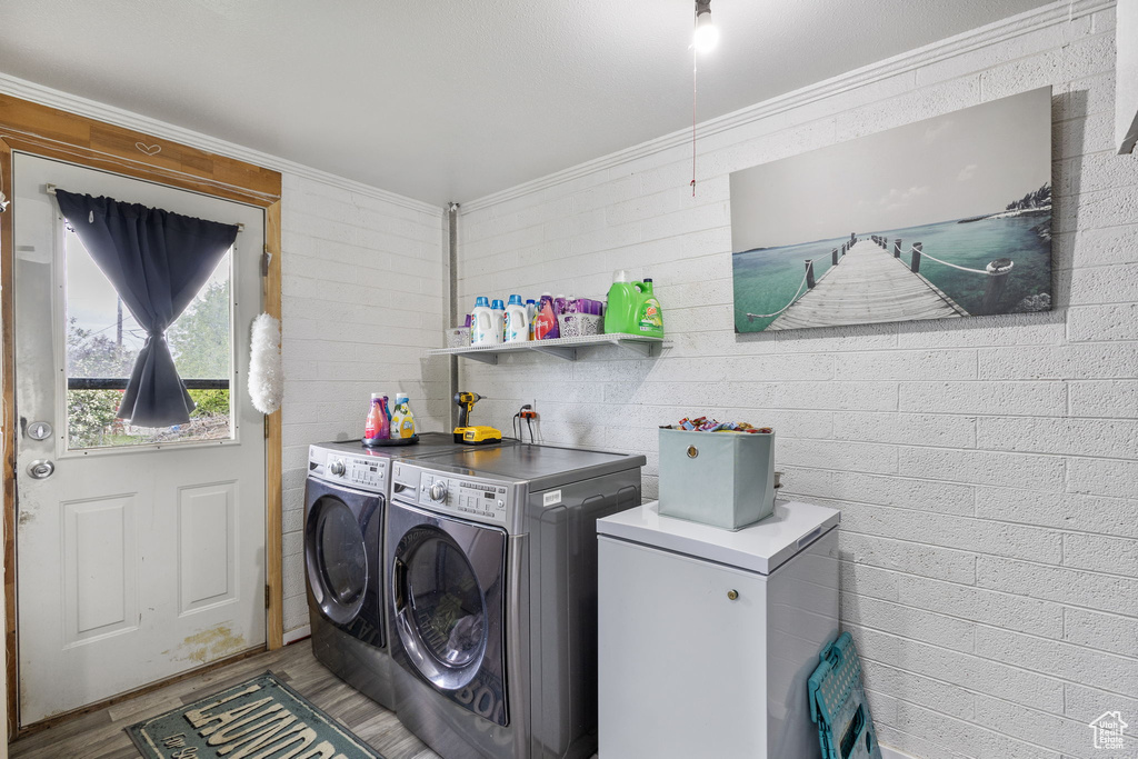 Laundry room with washing machine and clothes dryer, laundry area, crown molding, and wood finished floors