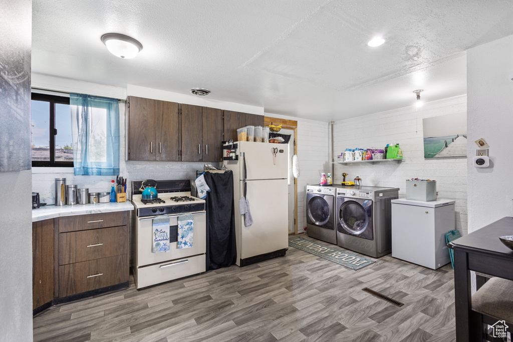 Kitchen with washer and dryer, dark brown cabinets, white appliances, light countertops, and light wood-type flooring