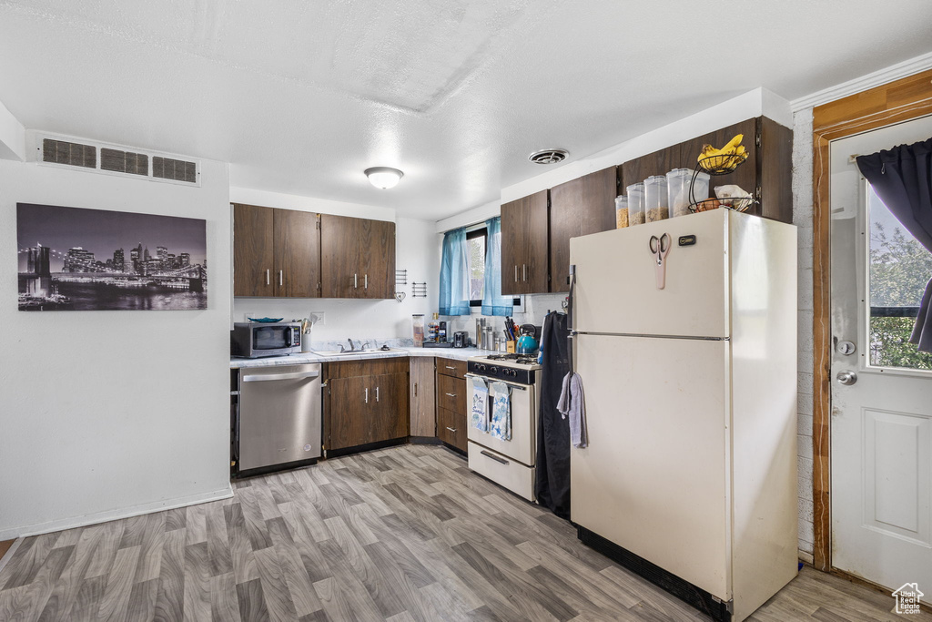 Kitchen featuring dark brown cabinetry, visible vents, appliances with stainless steel finishes, light countertops, and light wood-style flooring