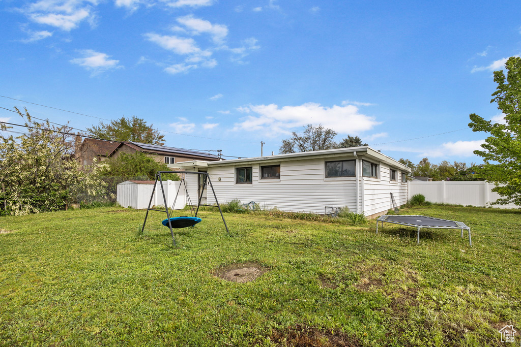 Rear view of property featuring a lawn, fence, a trampoline, and a playground