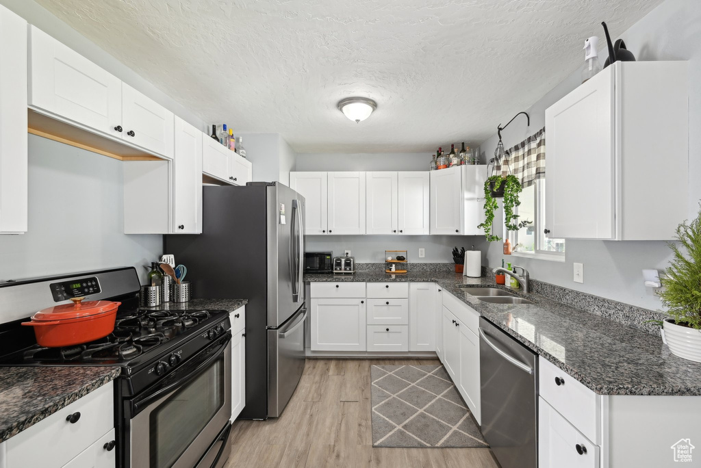 Kitchen with light wood-style floors, white cabinetry, a textured ceiling, a sink, and appliances with stainless steel finishes