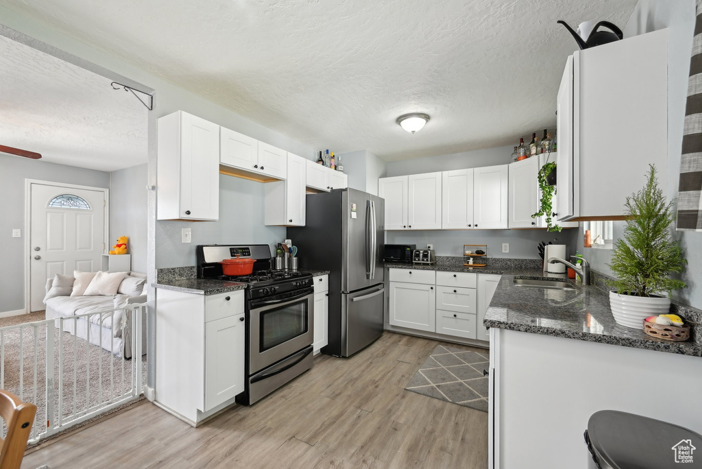 Kitchen featuring light wood-style floors, a textured ceiling, white cabinetry, dark stone countertops, and stainless steel appliances
