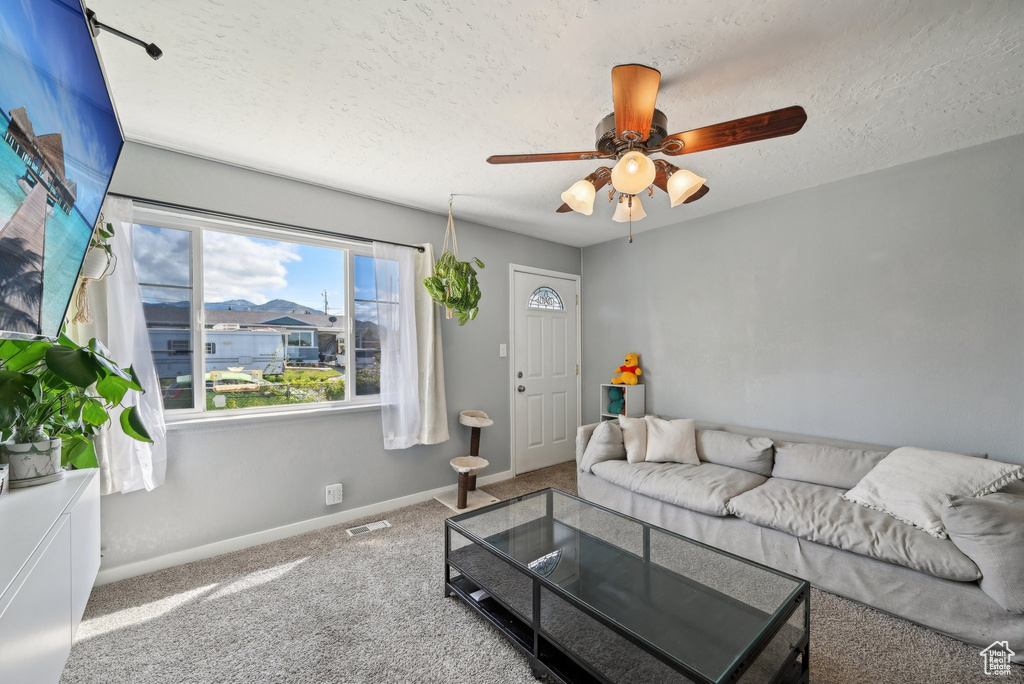 Living room with ceiling fan, a textured ceiling, visible vents, baseboards, and carpet