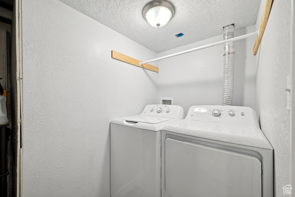 Washroom featuring separate washer and dryer, laundry area, a textured wall, and a textured ceiling