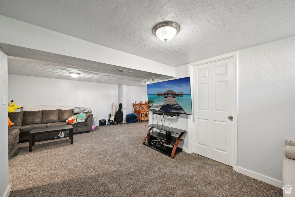 Carpeted living room featuring baseboards, a textured ceiling, and visible vents