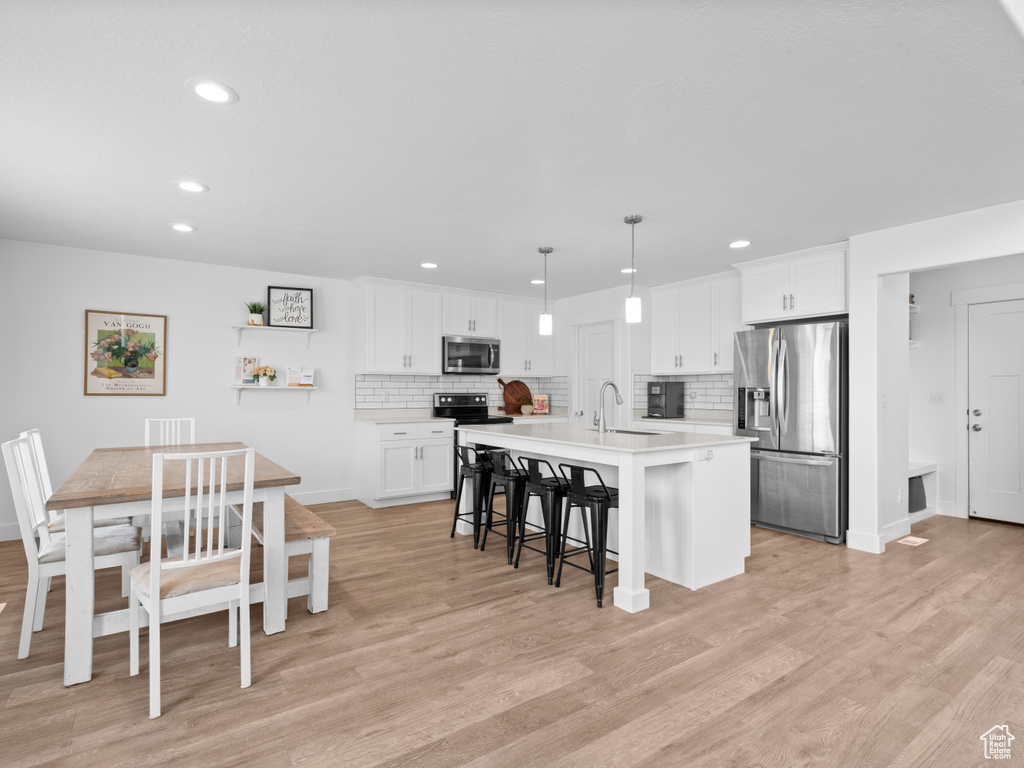 Kitchen with a kitchen breakfast bar, stainless steel appliances, recessed lighting, and light wood-style flooring