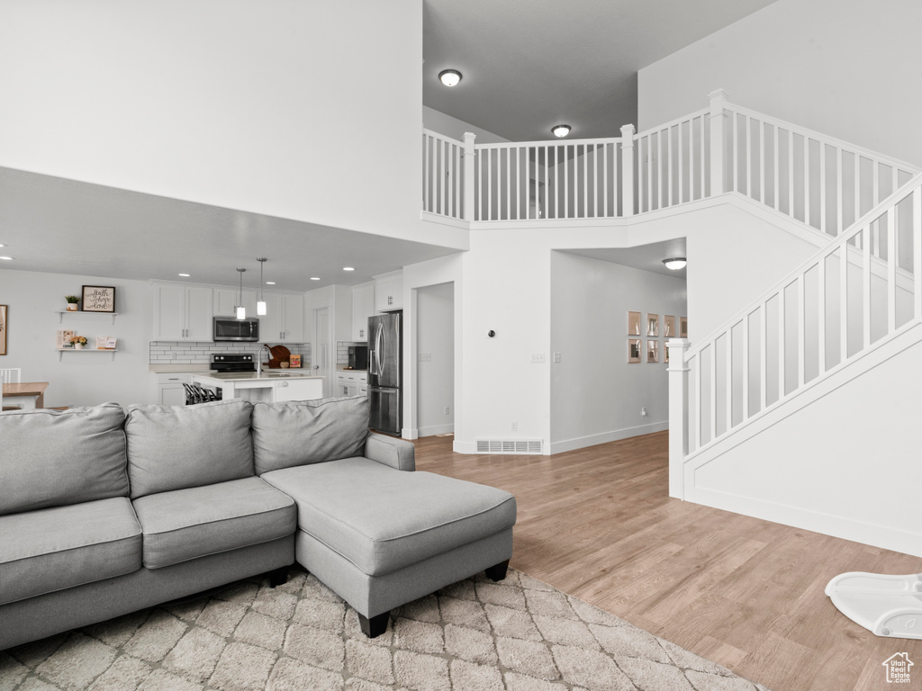 Living area with visible vents, a towering ceiling, stairway, baseboards, and light wood-style flooring