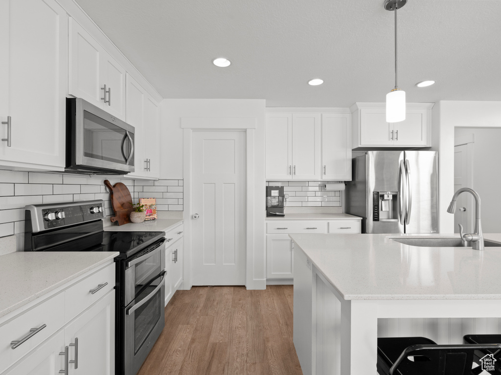 Kitchen with recessed lighting, tasteful backsplash, a sink, light wood finished floors, and stainless steel appliances