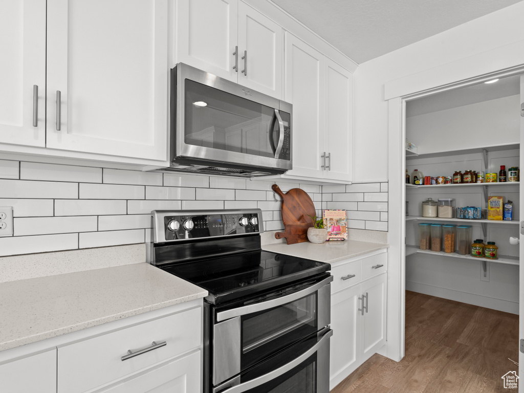 Kitchen with appliances with stainless steel finishes, white cabinets, decorative backsplash, and light wood-type flooring