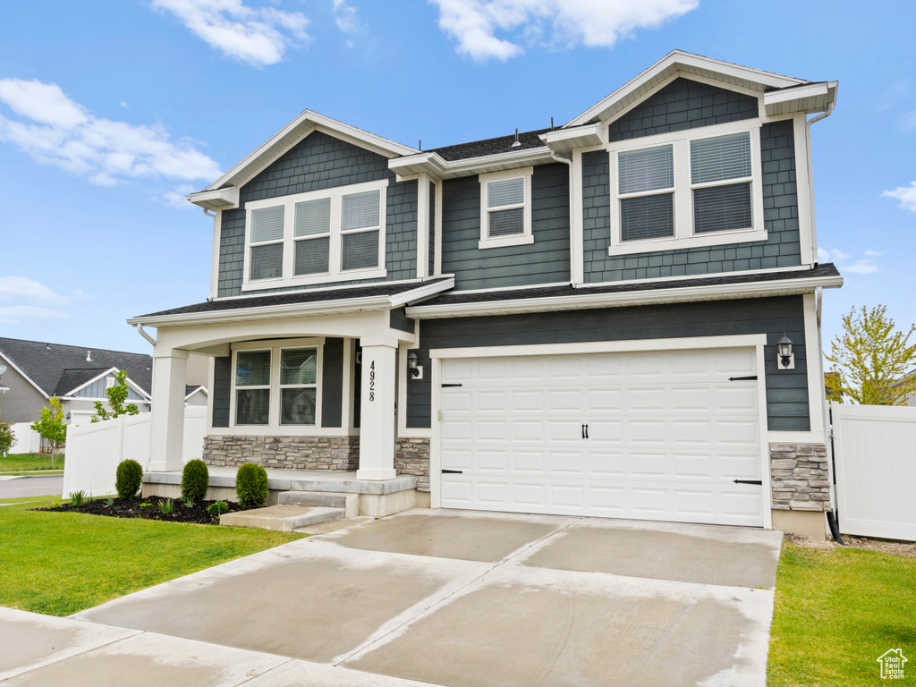 Craftsman-style home with driveway, a garage, fence, a front lawn, and stone siding