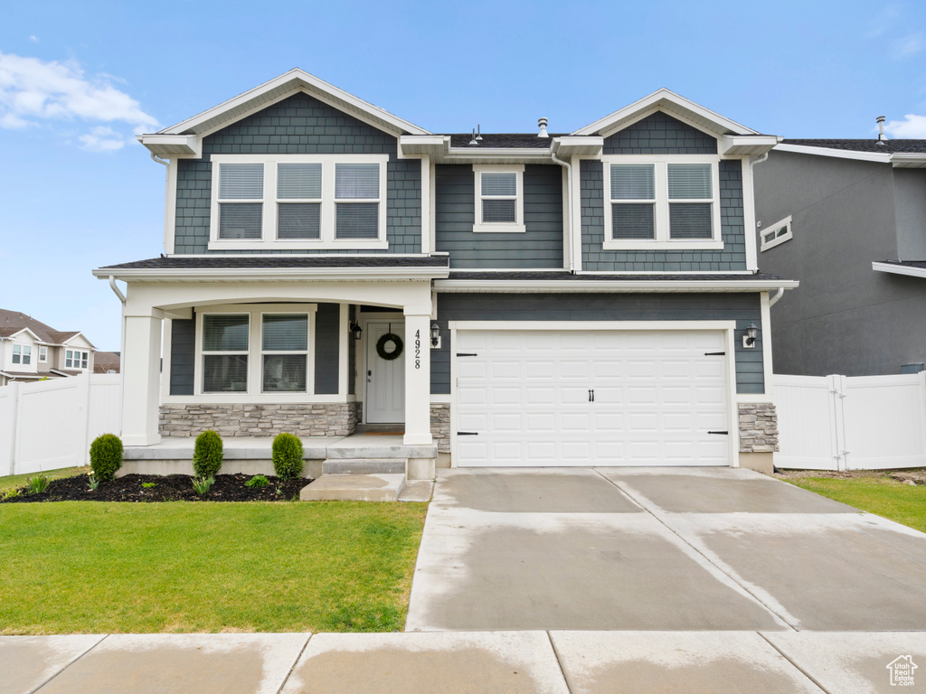 Craftsman house featuring covered porch, a front yard, a garage, fence, and stone siding