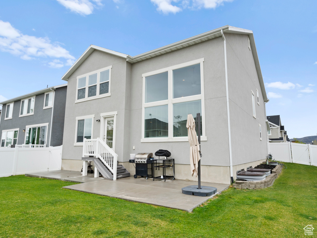 Rear view of property featuring stucco siding, a patio area, fence, and a lawn