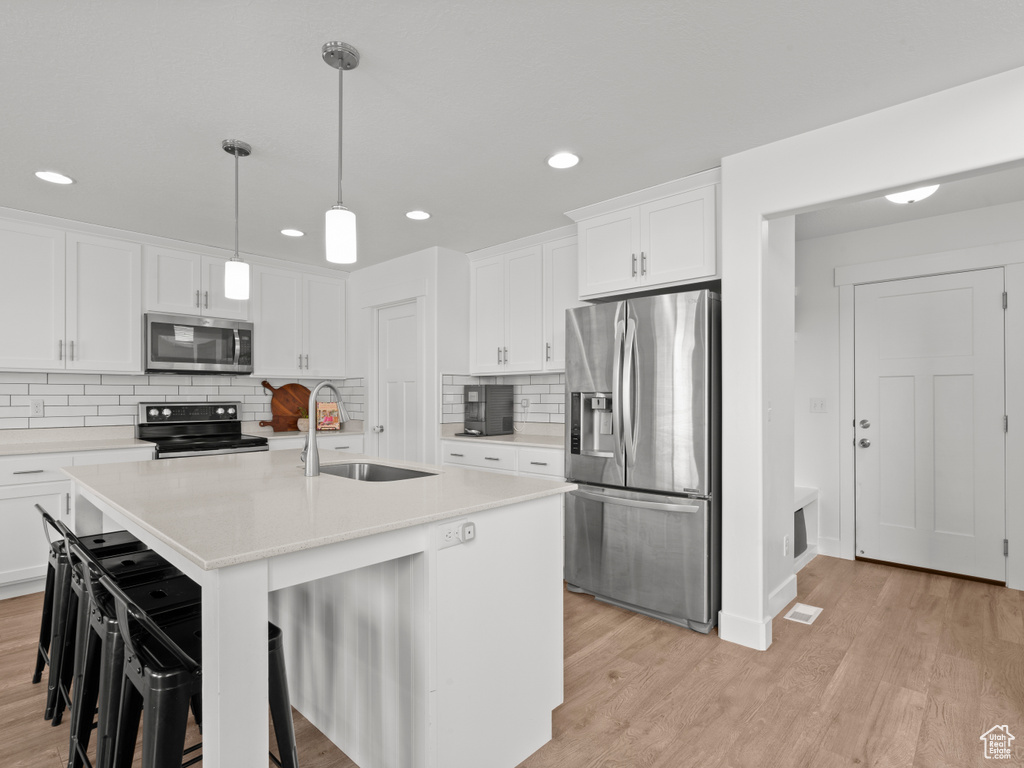 Kitchen with white cabinets, stainless steel appliances, a sink, and light wood-type flooring