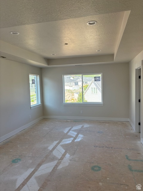 Spare room featuring a raised ceiling, a textured ceiling, baseboards, and recessed lighting