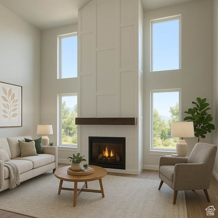 Living area with a high ceiling, light wood finished floors, healthy amount of natural light, and a tiled fireplace