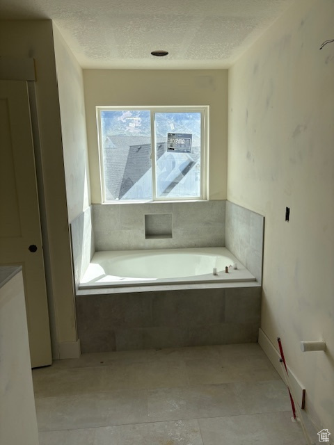 Bathroom with a textured ceiling, tile patterned flooring, and a bath