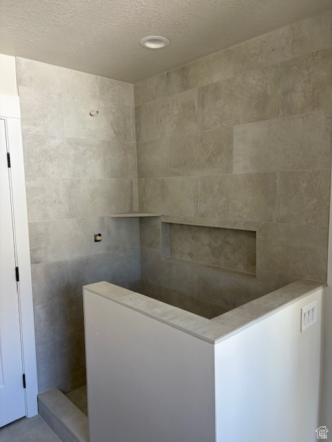 Bathroom featuring a textured ceiling and a tile shower