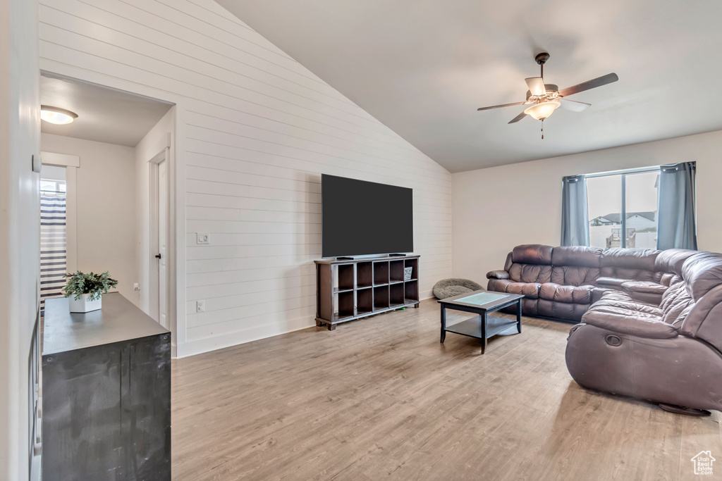 Living room featuring light wood-style floors, wood walls, a ceiling fan, and lofted ceiling
