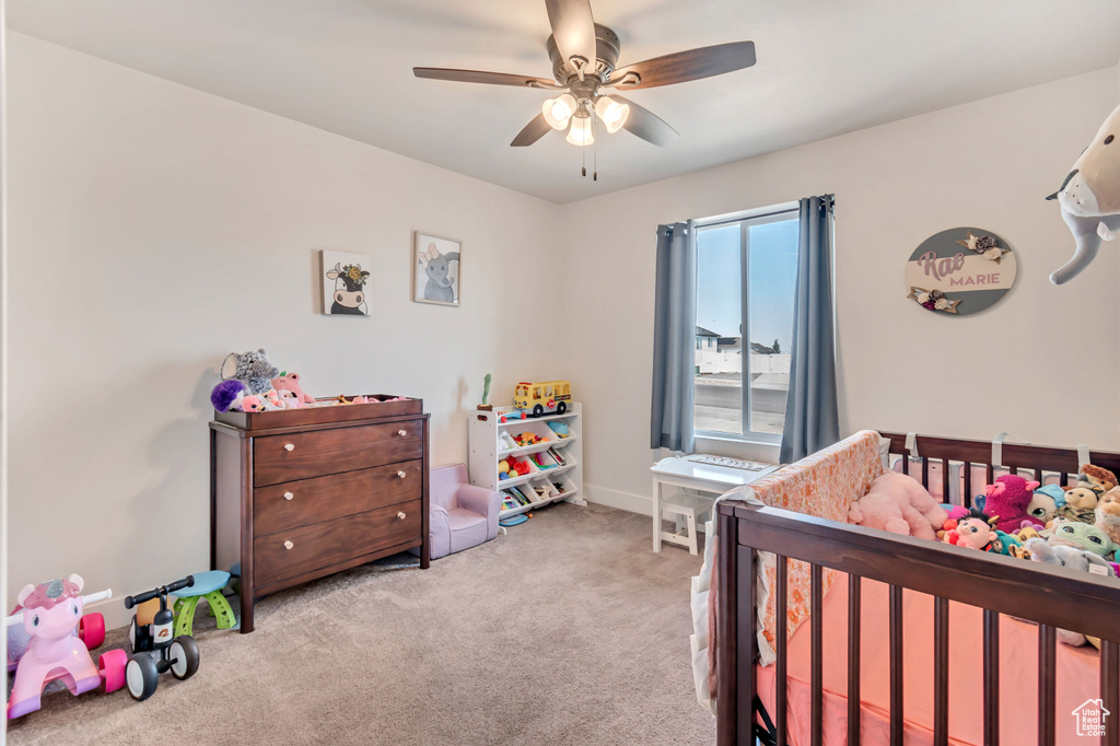 Carpeted bedroom featuring ceiling fan and a crib